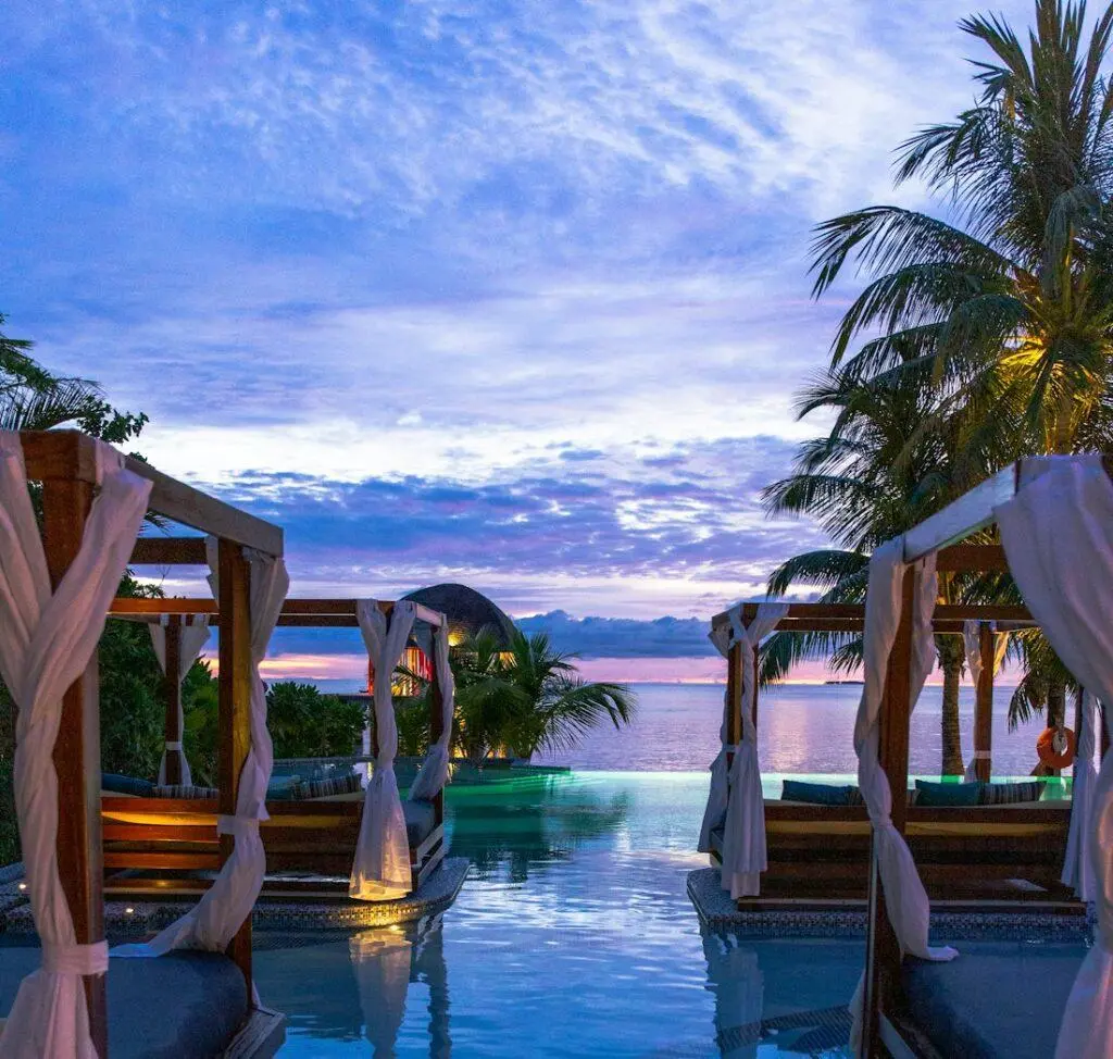 Seaside pool at sunset with draped pavilions and palm trees