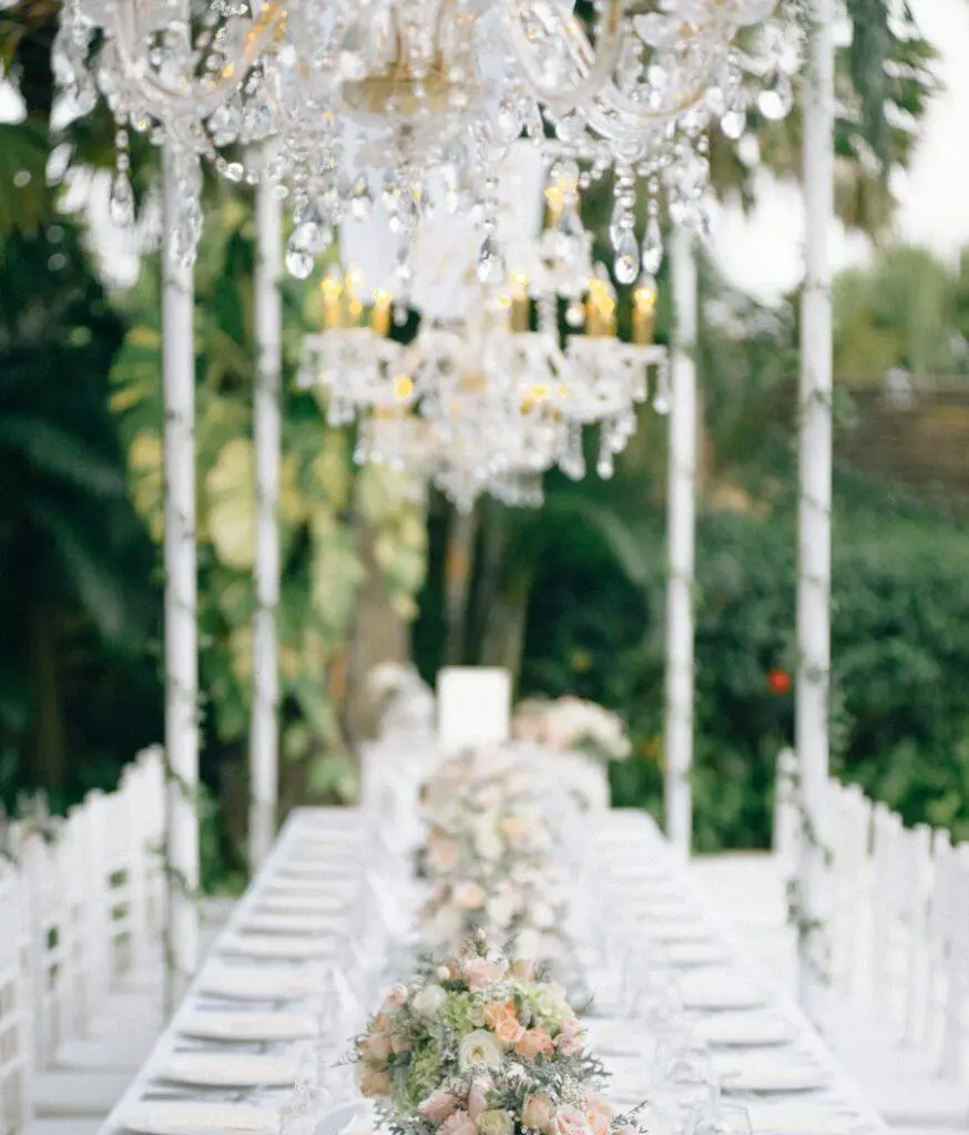 White floral aisle beneath crystal chandeliers in a glass venue